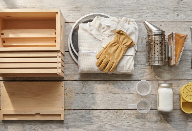 complete first-year beekeeping equipment list laid out with hive, suit, smoker, hive tool, and mite-test cup